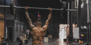 shirtless man in gym lifting dumbbells back