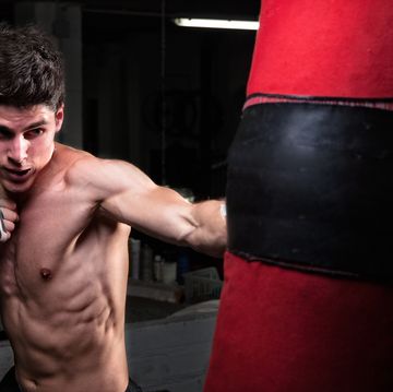 shirtless man punching bag in boxing rink