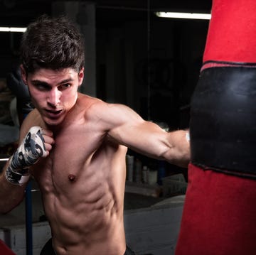 shirtless man punching bag in boxing rink