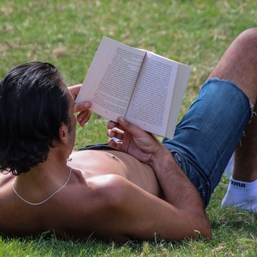 a shirtless man reads a book on the grass on a warm summer