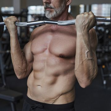 shirtless mature man exercising with barbell in gym