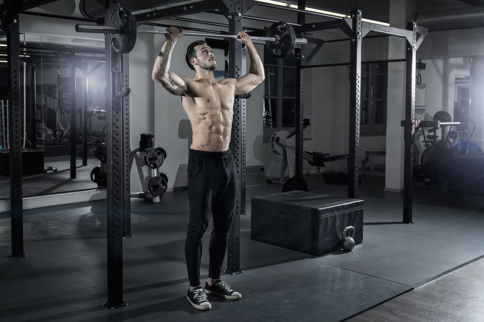 shirtless muscular man exercising with barbell at the gym