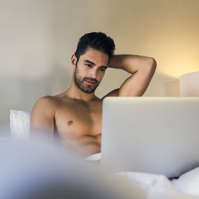 shirtless young man using laptop in bed