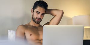 shirtless young man using laptop in bed