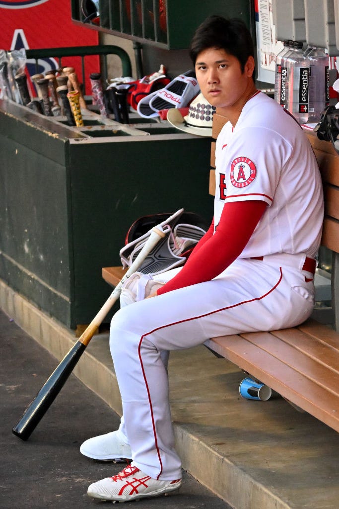 shohei ohtani sitting with his bat in the dugout