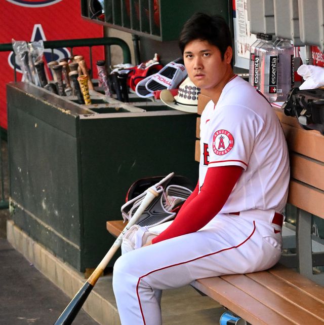 shohei ohtani sitting with his bat in the dugout