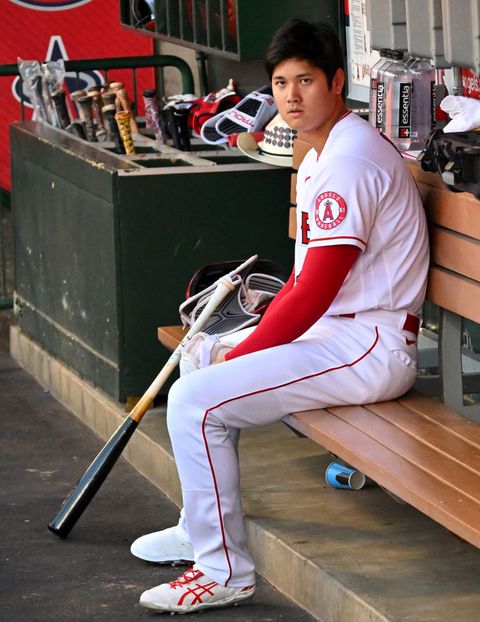 shohei ohtani sitting with his bat in the dugout