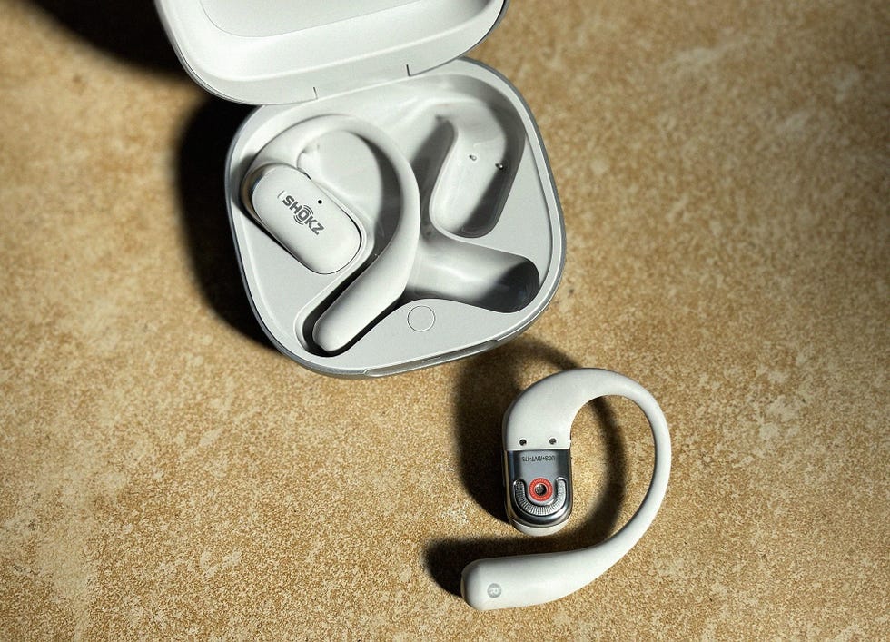 a pair of grey shokz open earbuds with one bud out of the case