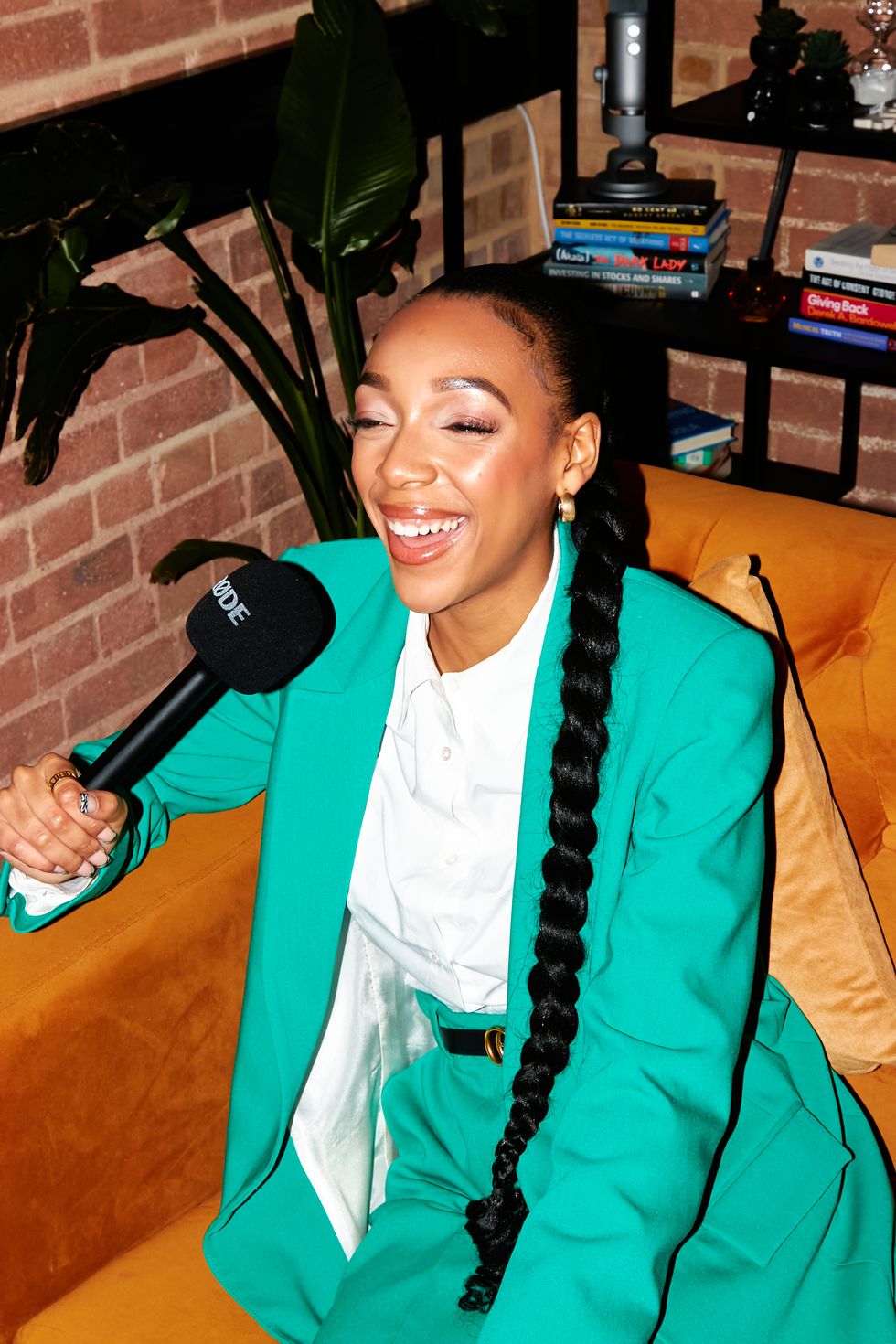 shola west pictured in green formal suit she smiles as she speaks into a microphone