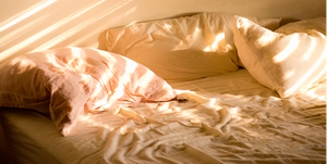a messy bed with sunlight beams shining in from the window