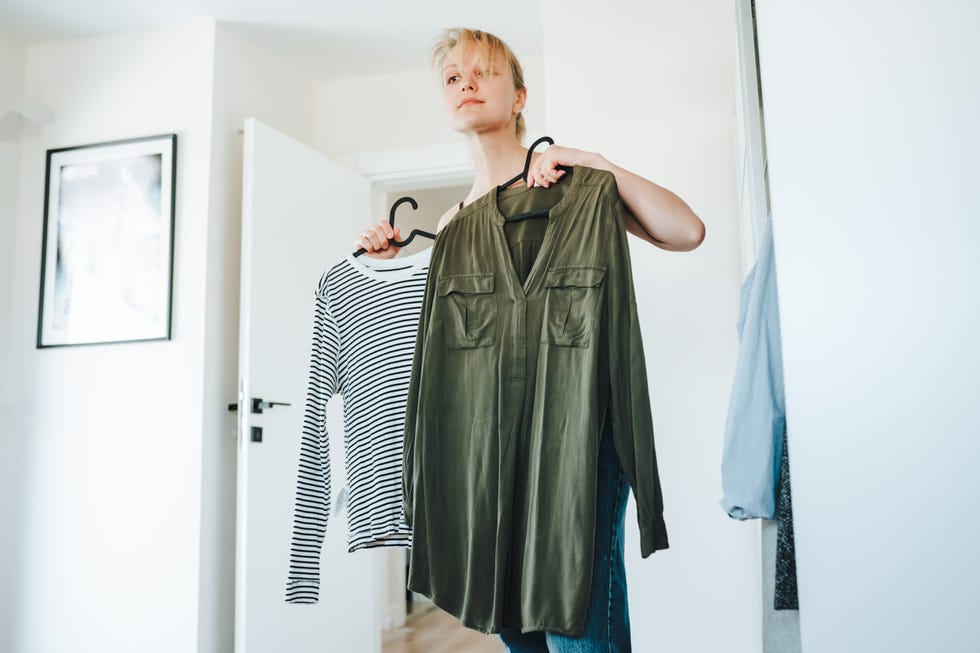 shopaholic problem and struggling to choose the outfit woman choosing fashion clothes outfit, holding racks with shirts in hands in bright living room