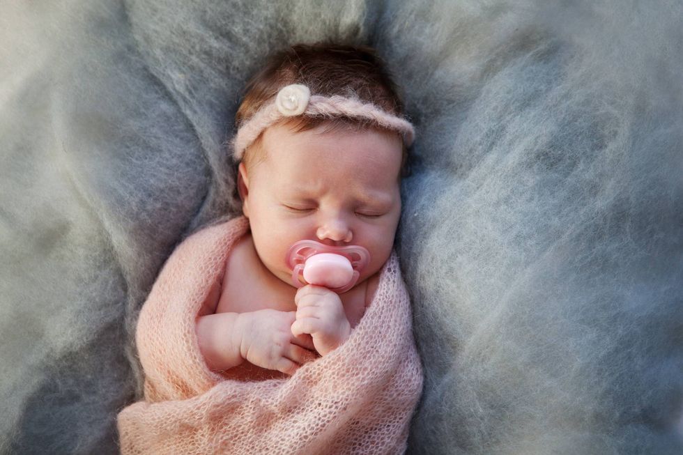 a sleeping baby uses a pacifier while wrapped in a pink blanket