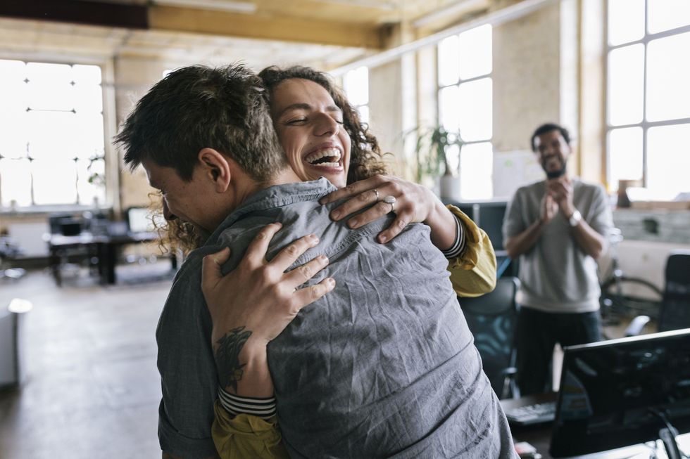 people in a startup business space celebrating a co worker woman is being hugged by one of her co worker