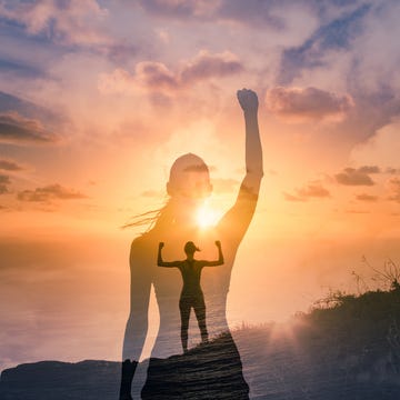 strong woman on a mountain flexing arms with fists in the air in front of sunset