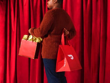 person holding two red bags with a curtain backdrop