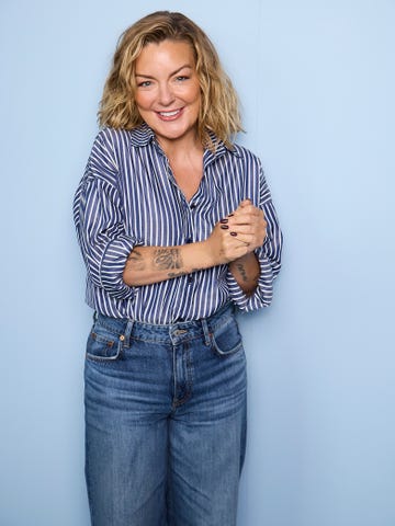 individual wearing a striped shirt and jeans standing against a light blue backdrop