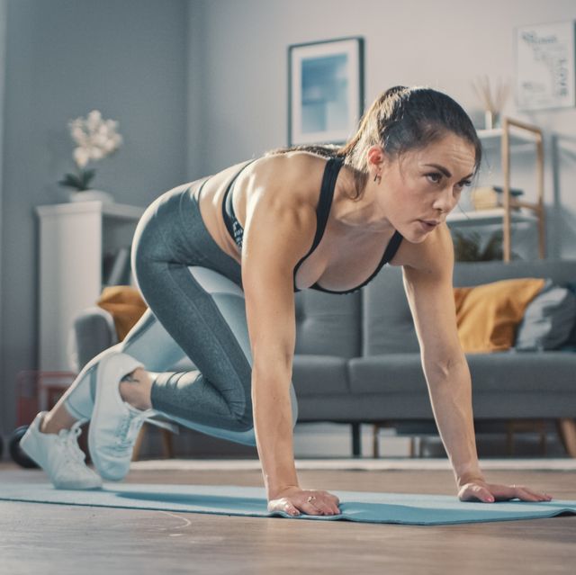 shot of a beautiful confident strong fitness female in a grey athletic outfit is doing mountain climber exercises in her bright and spacious apartment with cozy minimalistic interior
