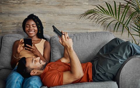 shot of a young couple lounging in the living room at home and using technology