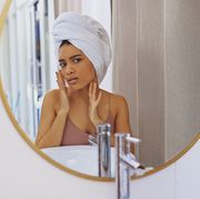 young woman inspecting her face in the bathroom mirror how to get rid of whiteheads