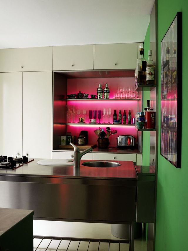 White and stainless steel kitchen with green wall and fuchsia and neon lined alcove shelving