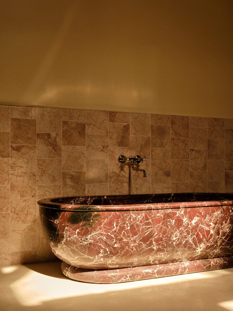 veined marble bathtub in orange-brown color, underneath a shiny faucet