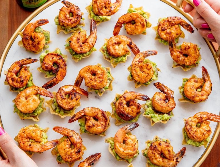 tortilla cups filled with guacamole and topped with spicy tails on shrimp
