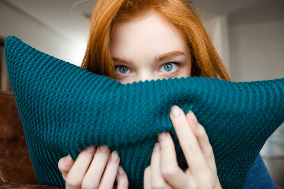 shy pretty young woman  hiding face behind knitted pillow