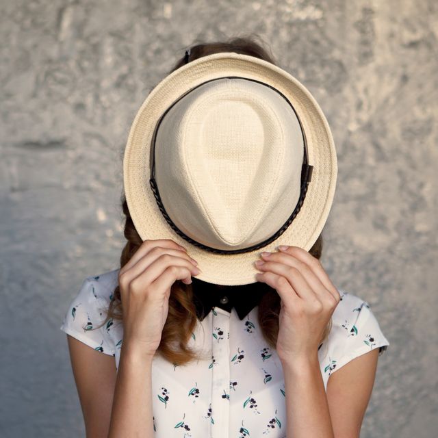 shy woman hiding behind hat