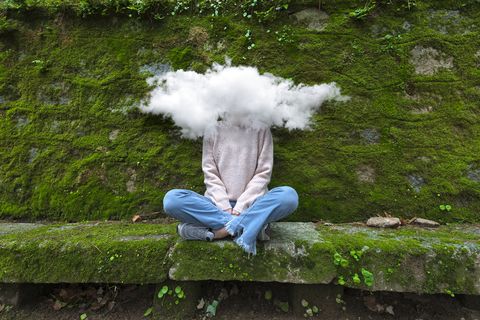 woman sitting on rock with a cloud over her face