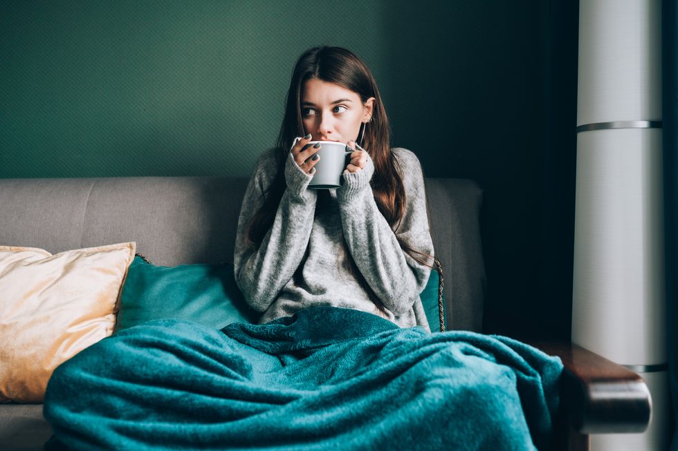 sick leave and seasonal indisposition at home young woman drink hot tea, wrapped in blanket in cold apartment