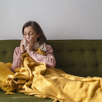 sick woman blowing nose in facial tissue at home