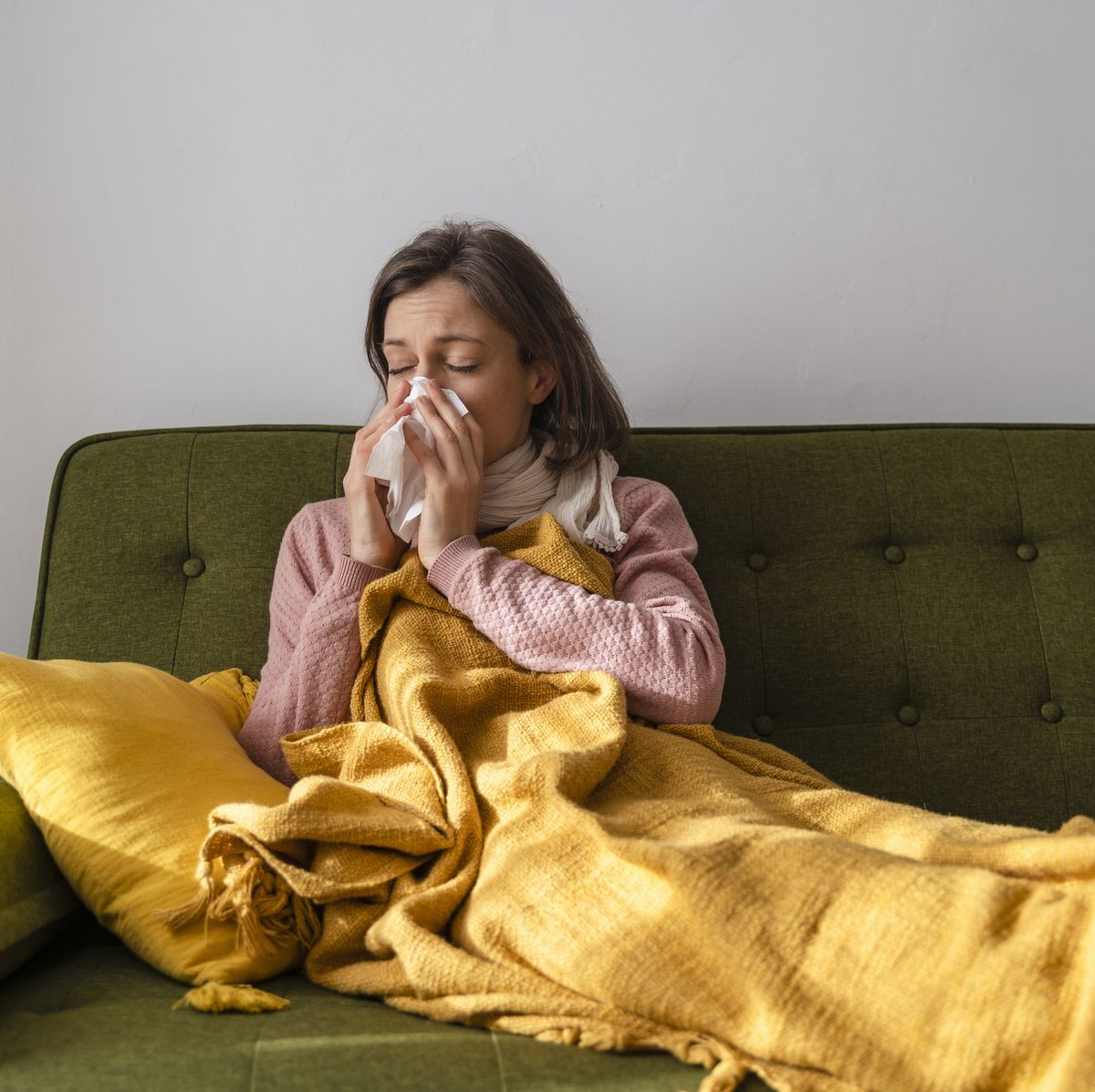 sick woman blowing nose in facial tissue at home