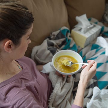 Sick woman eating soup on sofa