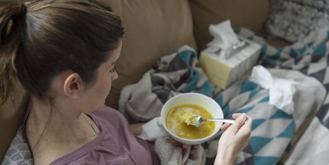 Sick woman eating soup on sofa