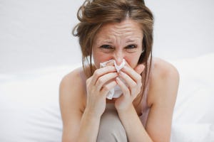 sick woman in bed blowing nose