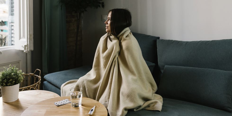 sick woman looking away while wrapped in blanket at home