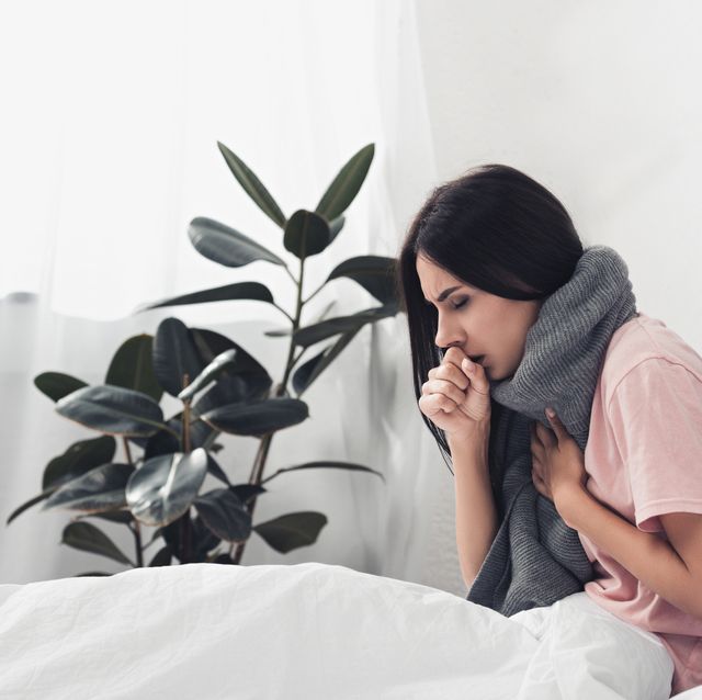 sick young woman sitting in bed and having cough while suffering from sore throat