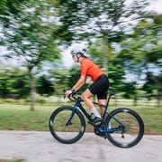side view asian chinese female professional cyclist athlete sportsman sprinting cycling in public park