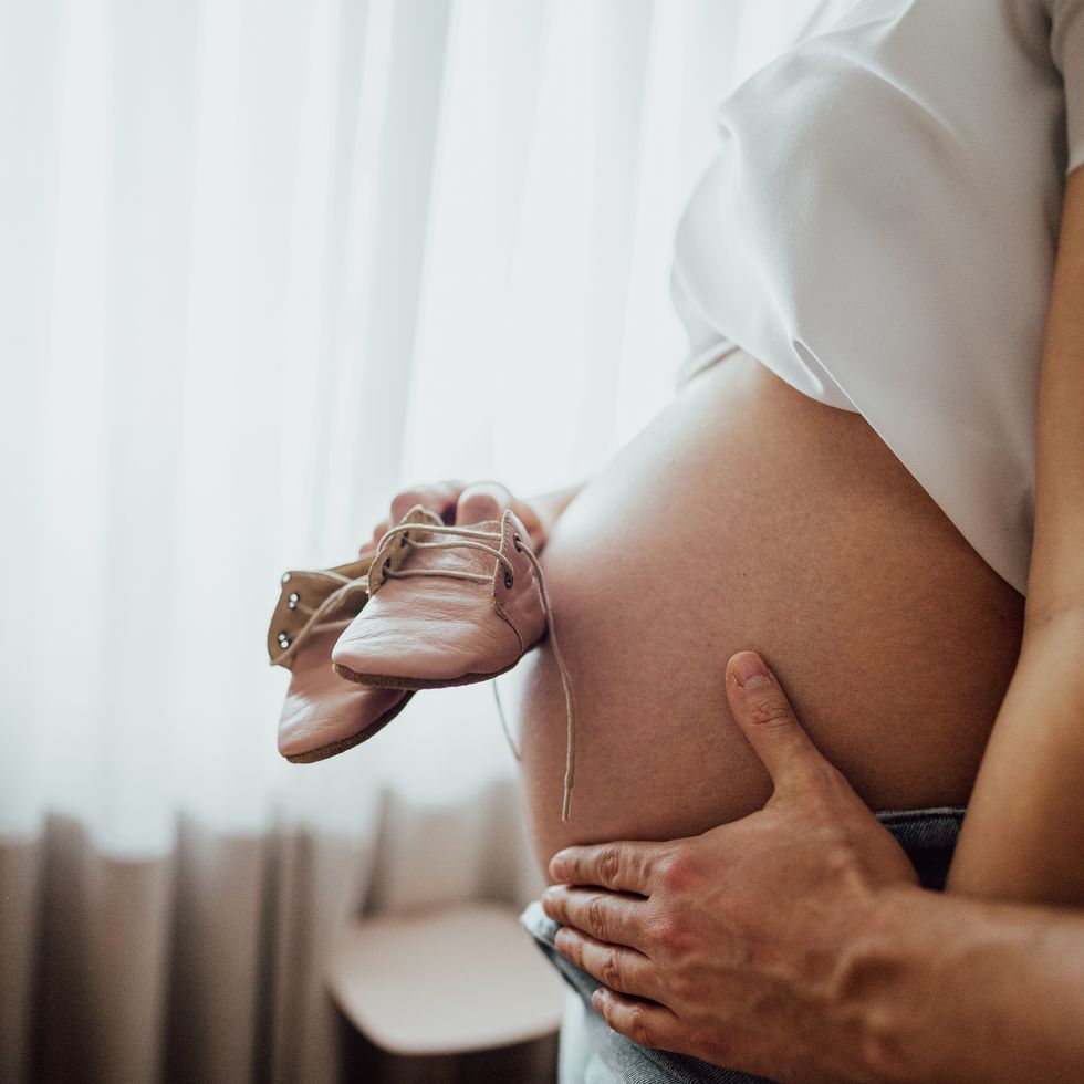 Side view of a person who touches the belly of a pregnant woman who holds home boats in the bedroom of the nursery at home