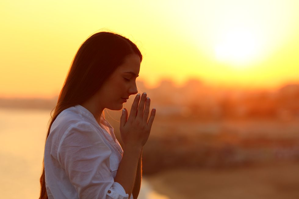 Side view of a woman praying at sunset