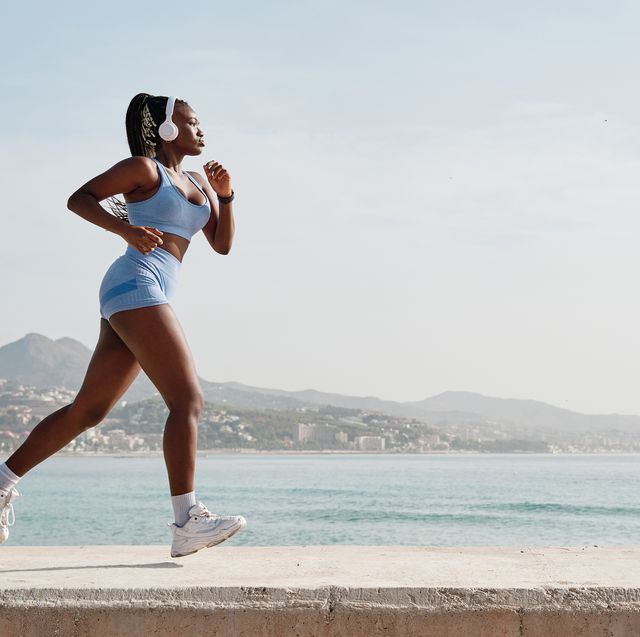 side view of a young black female athlete running on a stone wall with the coast in the background