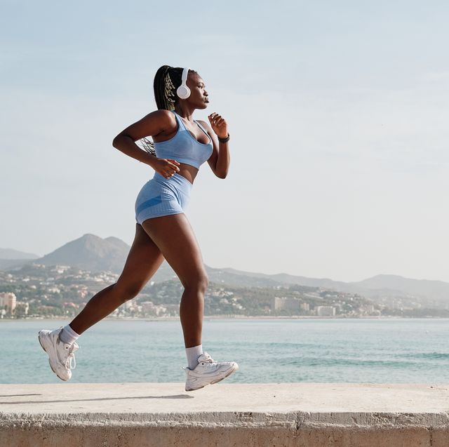 side view of a young black female athlete running on a stone wall with the coast in the background