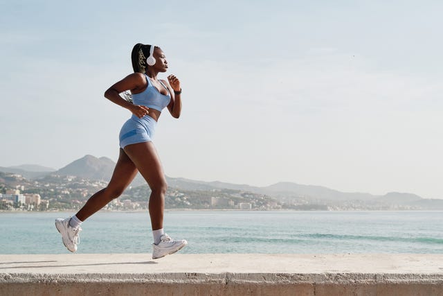 side view of a young black female athlete running on a stone wall with the coast in the background