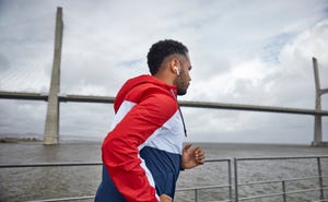 side view of african american man with earphones running near river bridge