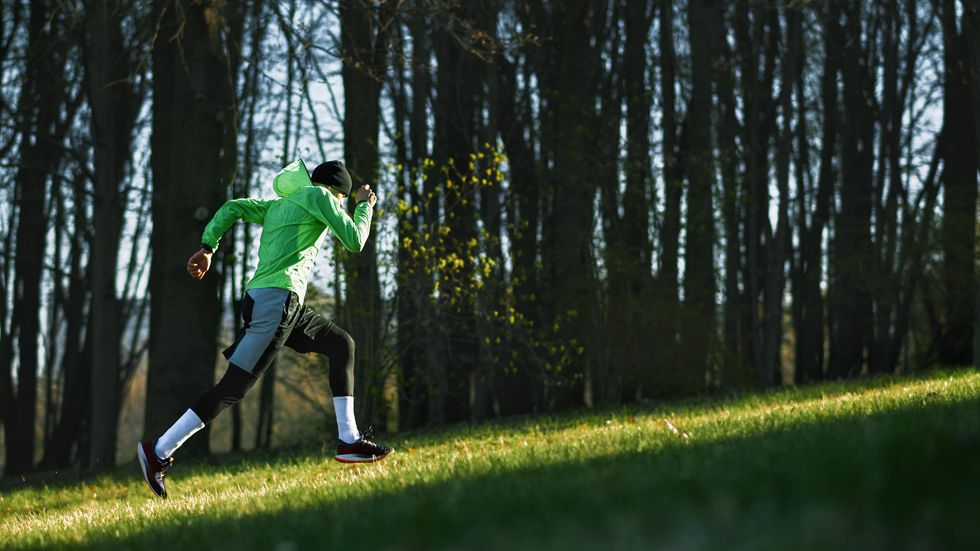side view of an athlete young man running on a hill in mountain athletic male jogging in the park in the morning in a sunny day people, healthy lifestyle and sport concept