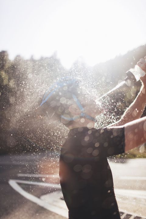 Side view of cyclist spraying water on face in sunny day