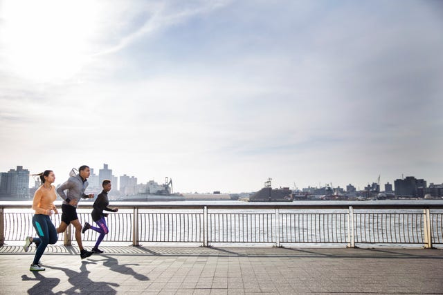side view of determined athletes running on footpath by river against sky