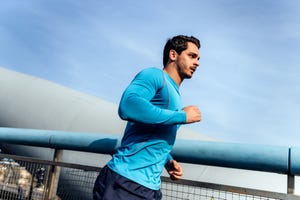 side view of determined young man jogging in city against sky