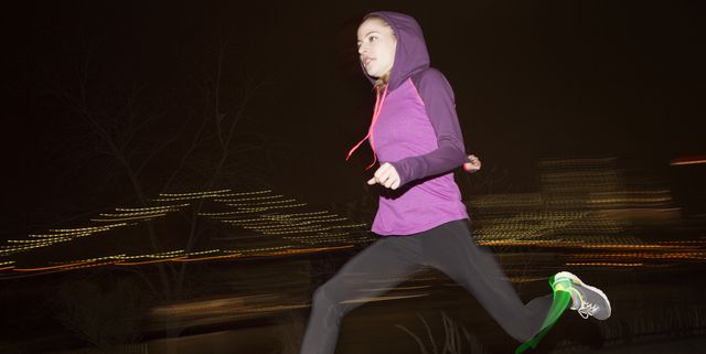 Side view of female jogger wearing hood while running on field at night