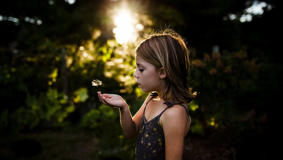 side view of girl blowing dandelion seed while standing at yard